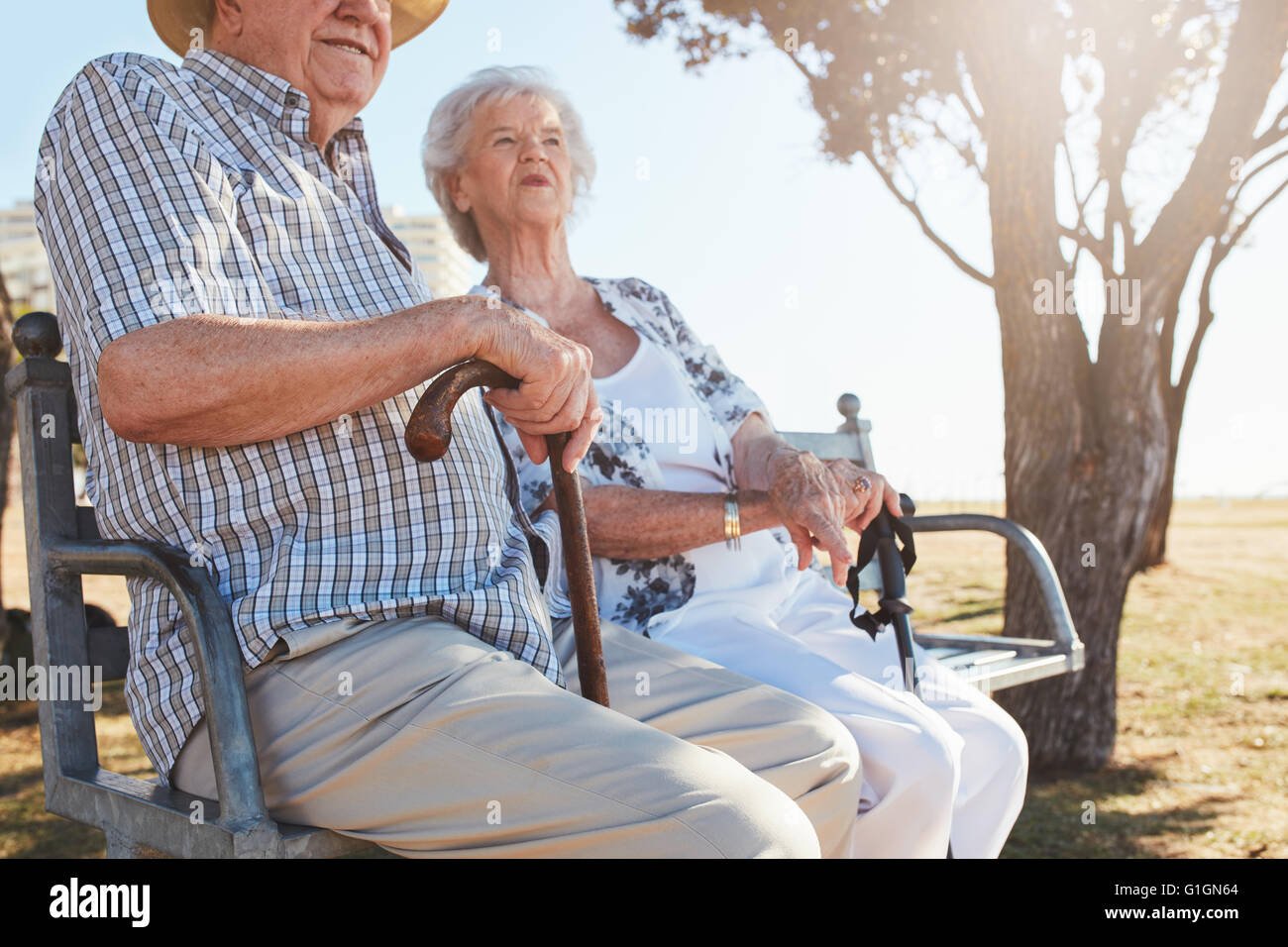 Couple assis sur un banc de parc avec bâton de marche. Vieux couple de détente en plein air sur une journée d'été. Banque D'Images