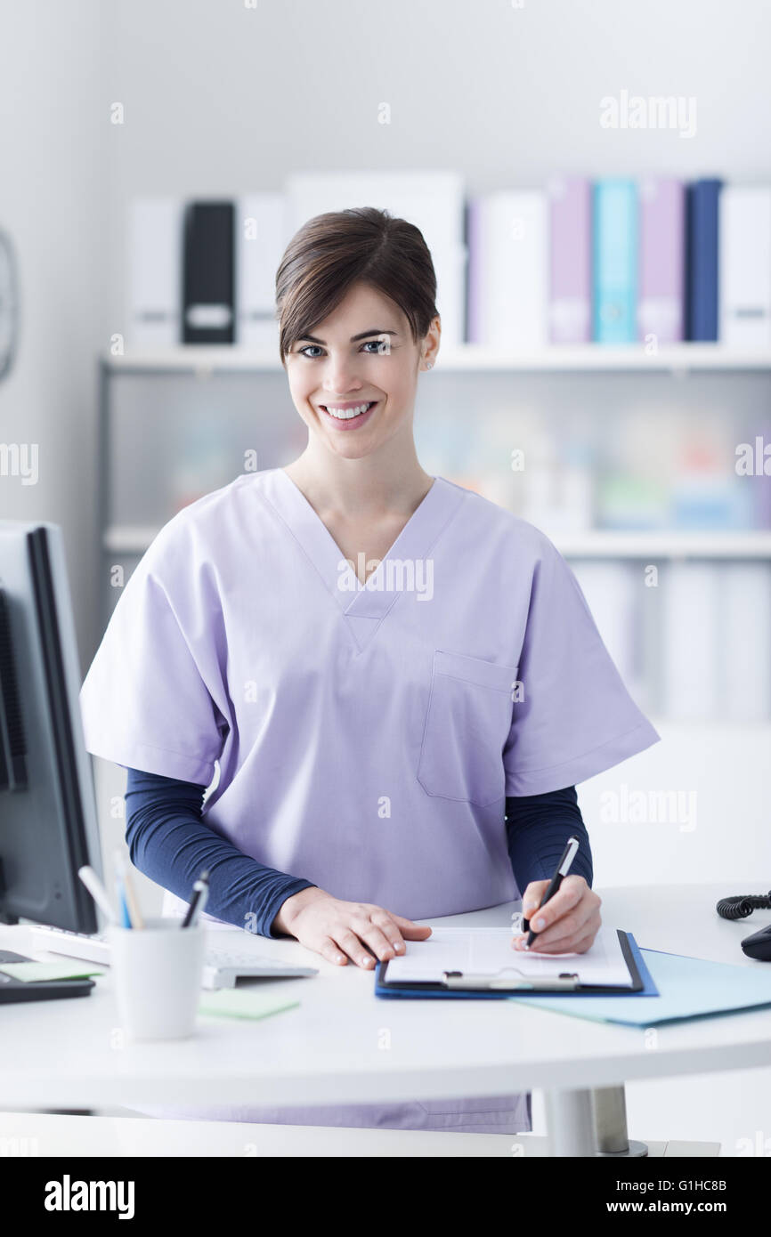 Médecin femme portant un maquis et travaillant à l'hôpital la réception, elle est l'écriture d'un rapport médical sur un presse-papiers et Banque D'Images