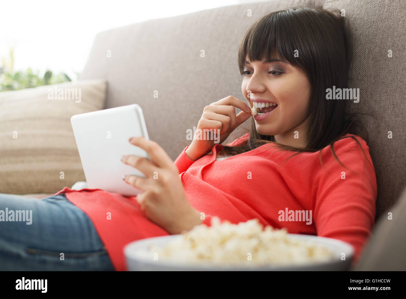 Jolie femme détente sur le canapé à la maison, c'est de regarder des vidéos en ligne et eating popcorn, streaming films concept Banque D'Images