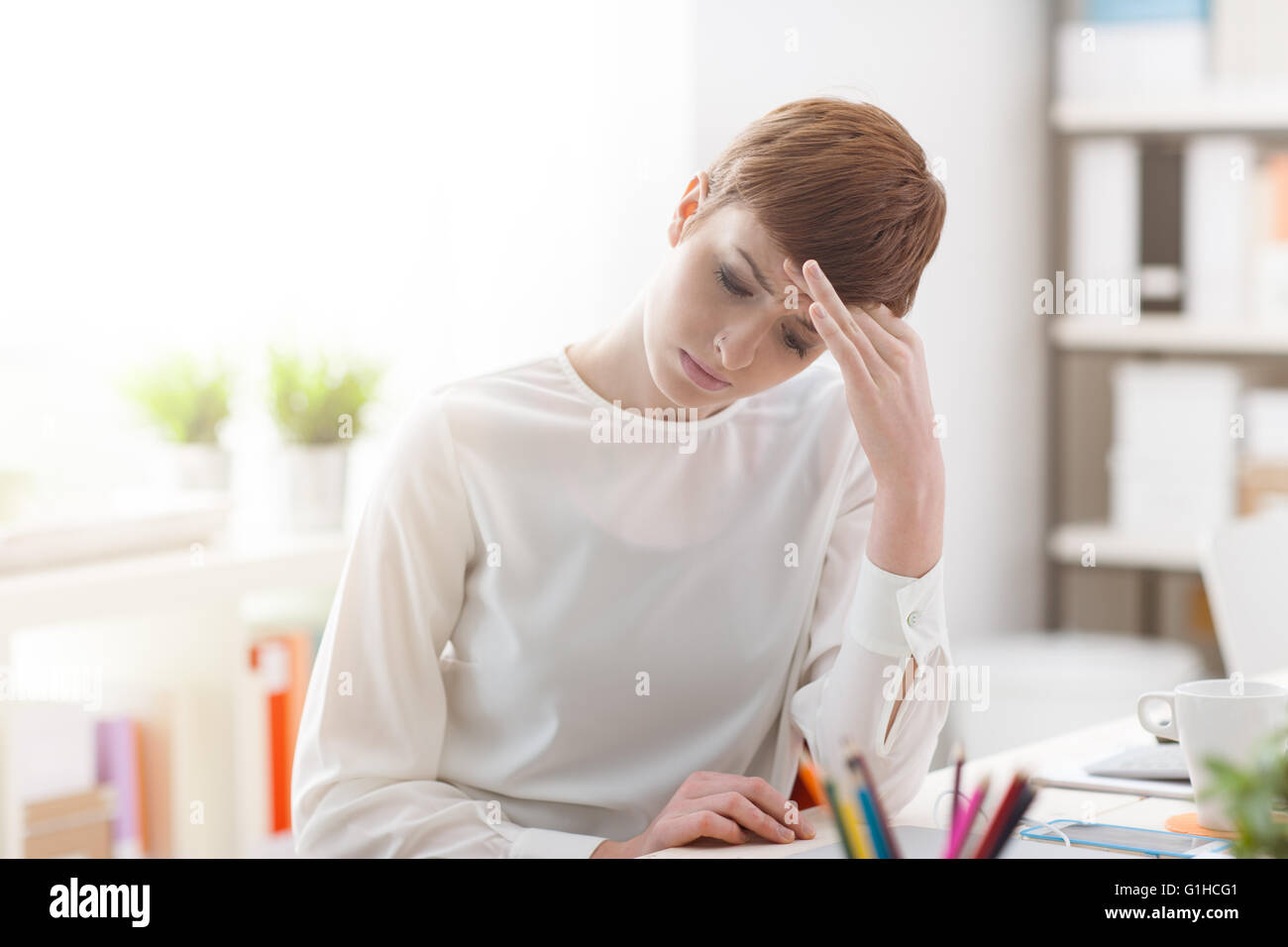 Fatigué businesswoman sitting at Office 24 et avoir un mal de tête, elle est en contact avec son front, le stress et la maladie concept Banque D'Images
