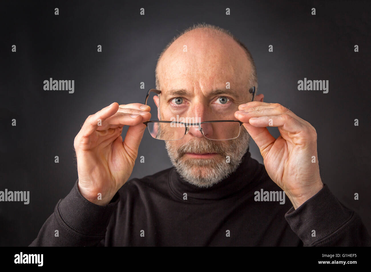Regarder au-dessus de lunettes de lecture - portrait de 60 ans homme barbu sur un fond noir Banque D'Images
