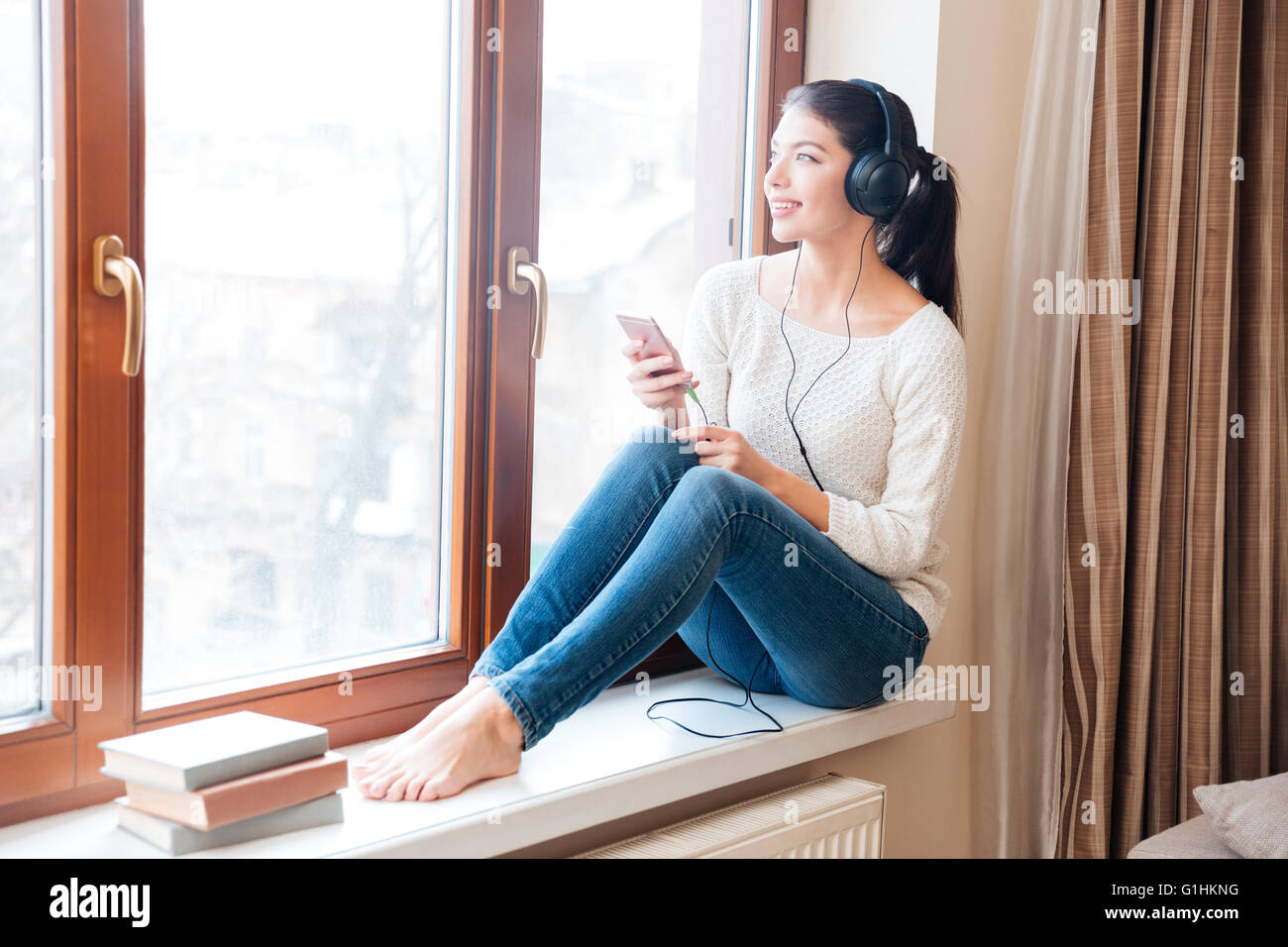 Happy woman sitting on windowsill et écoute la musique au casque à la maison Banque D'Images
