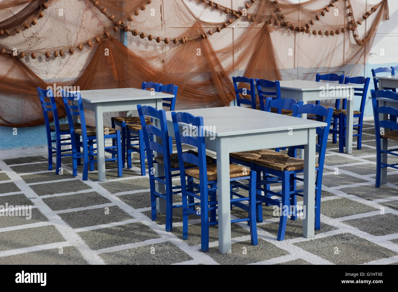 Tables vides arrangement et filets de pêche suspendus décoration murale de Glaros restaurant dans le quai de Myrina, Lemnos, Grèce Banque D'Images