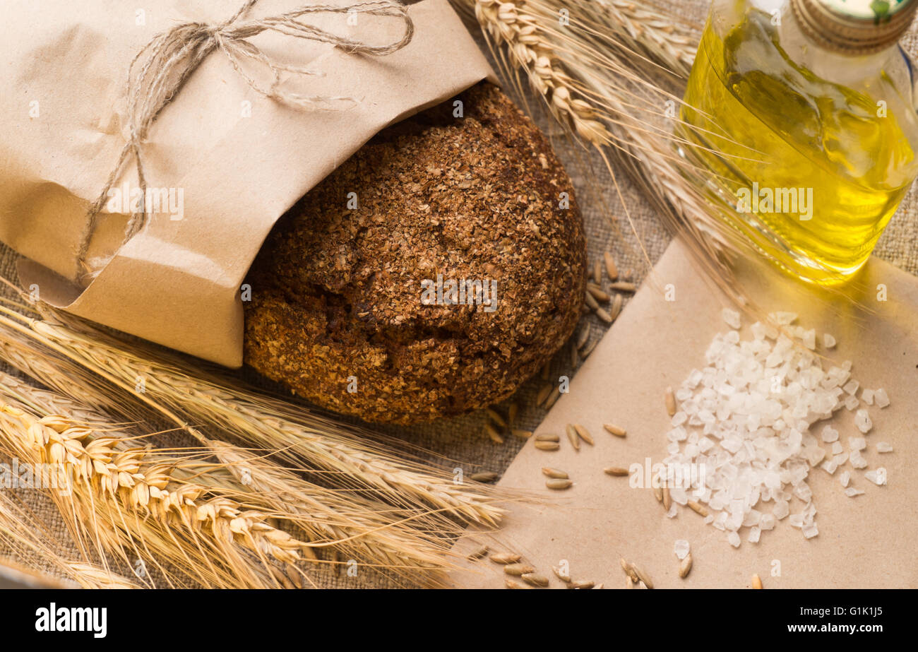 Le pain de seigle dans un sac en papier, les oreilles, une bouteille en verre avec de l'huile végétale, du sel et du grain sur le sac. Banque D'Images