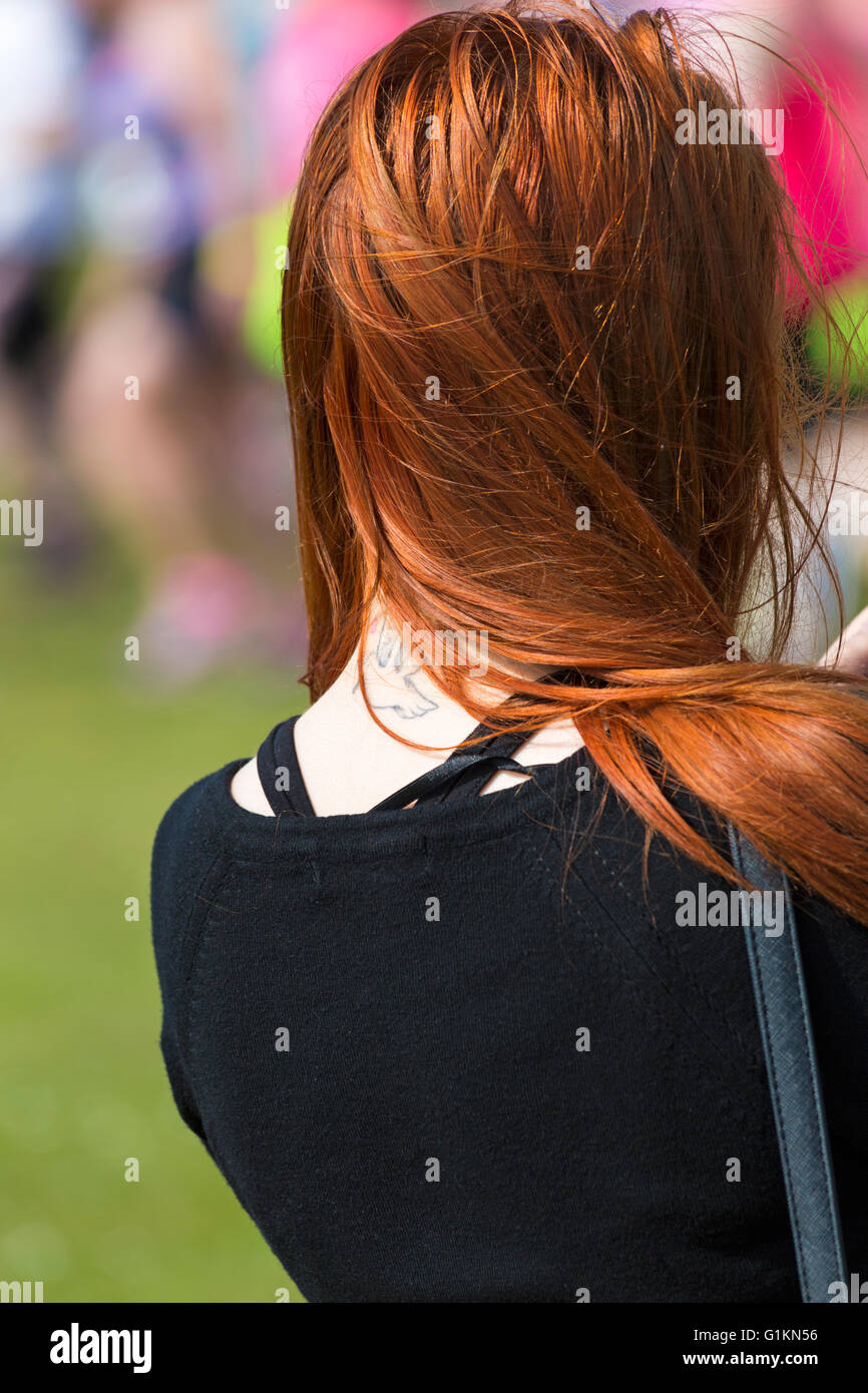 Jeune femme avec de longs cheveux de gingembre avec du vent qui souffle les cheveux pour révéler oiseau volant tattoo à événement sur Poole Banque D'Images