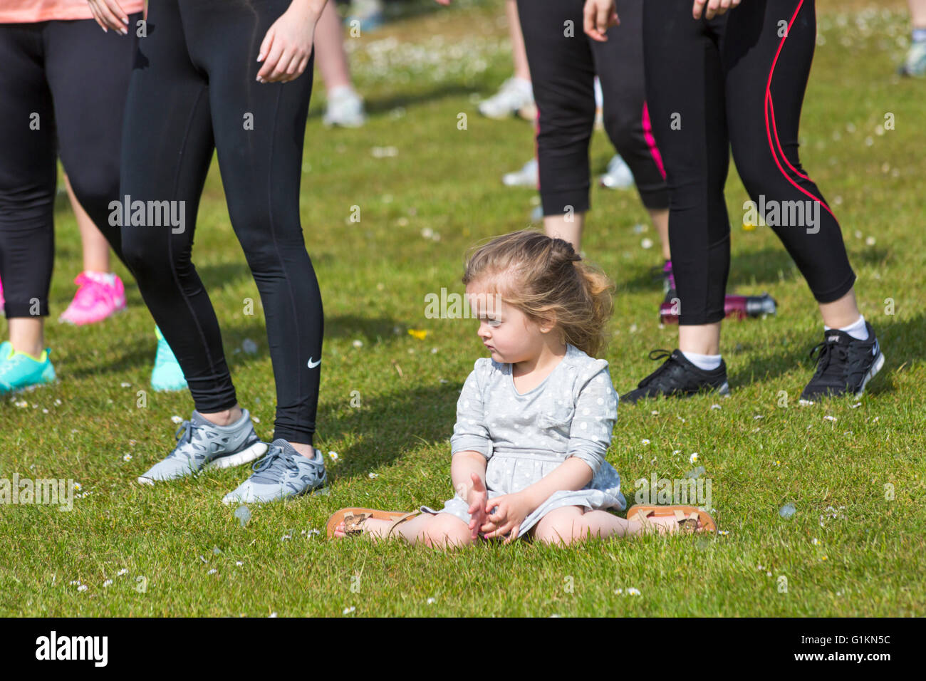 Jeune fille assise sur l'herbe tandis que les adultes autour d'elle de faire l'exercice et pour l'événement à Poole Banque D'Images