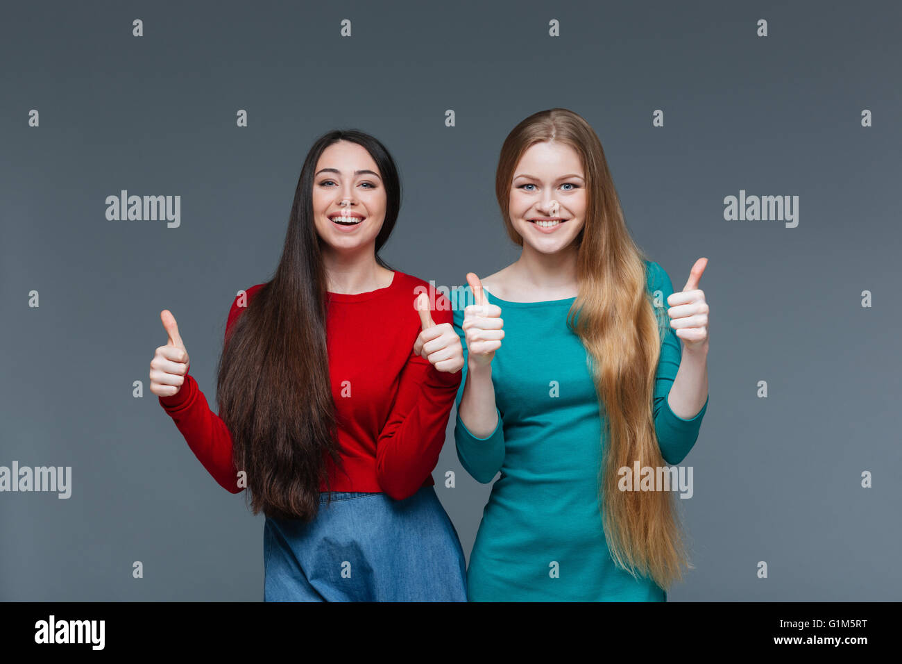 Deux heureux filles showing Thumbs up sur fond gris Banque D'Images