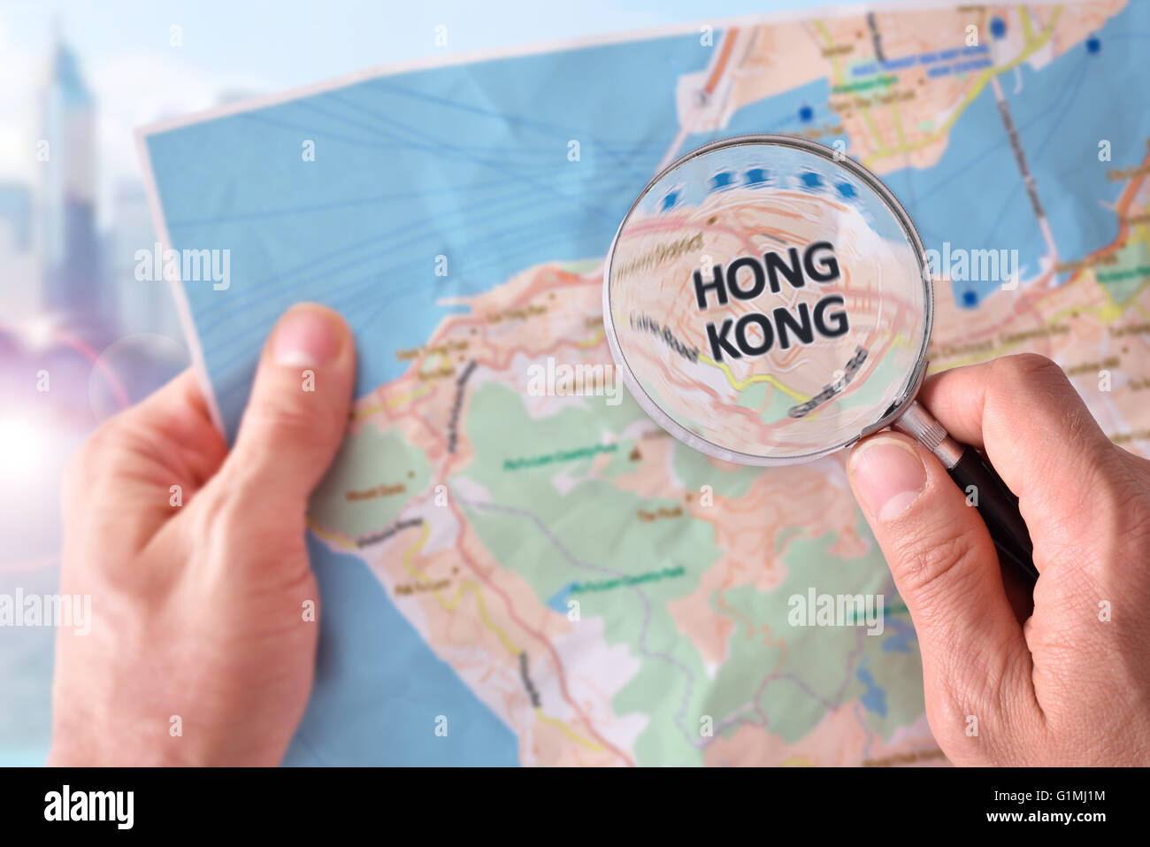 Mains de ramasser une carte de Hong Kong et à la recherche d'un endroit à l'aide d'une loupe avec les gratte-ciel dans la bac Banque D'Images