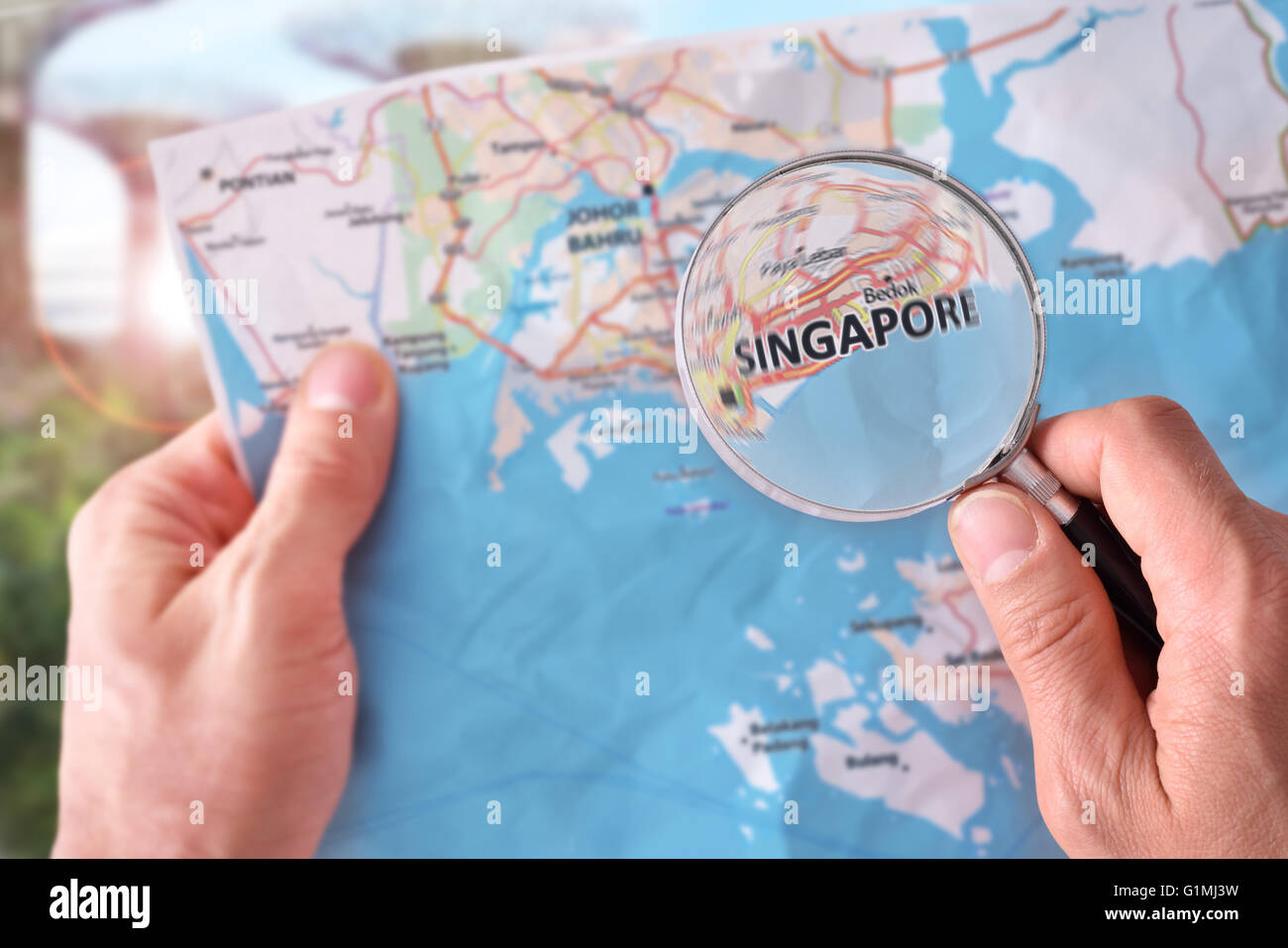 Mains de ramasser une carte de Singapour et à la recherche d'un endroit à l'aide d'une loupe avec un représentant dans le monument backg Banque D'Images