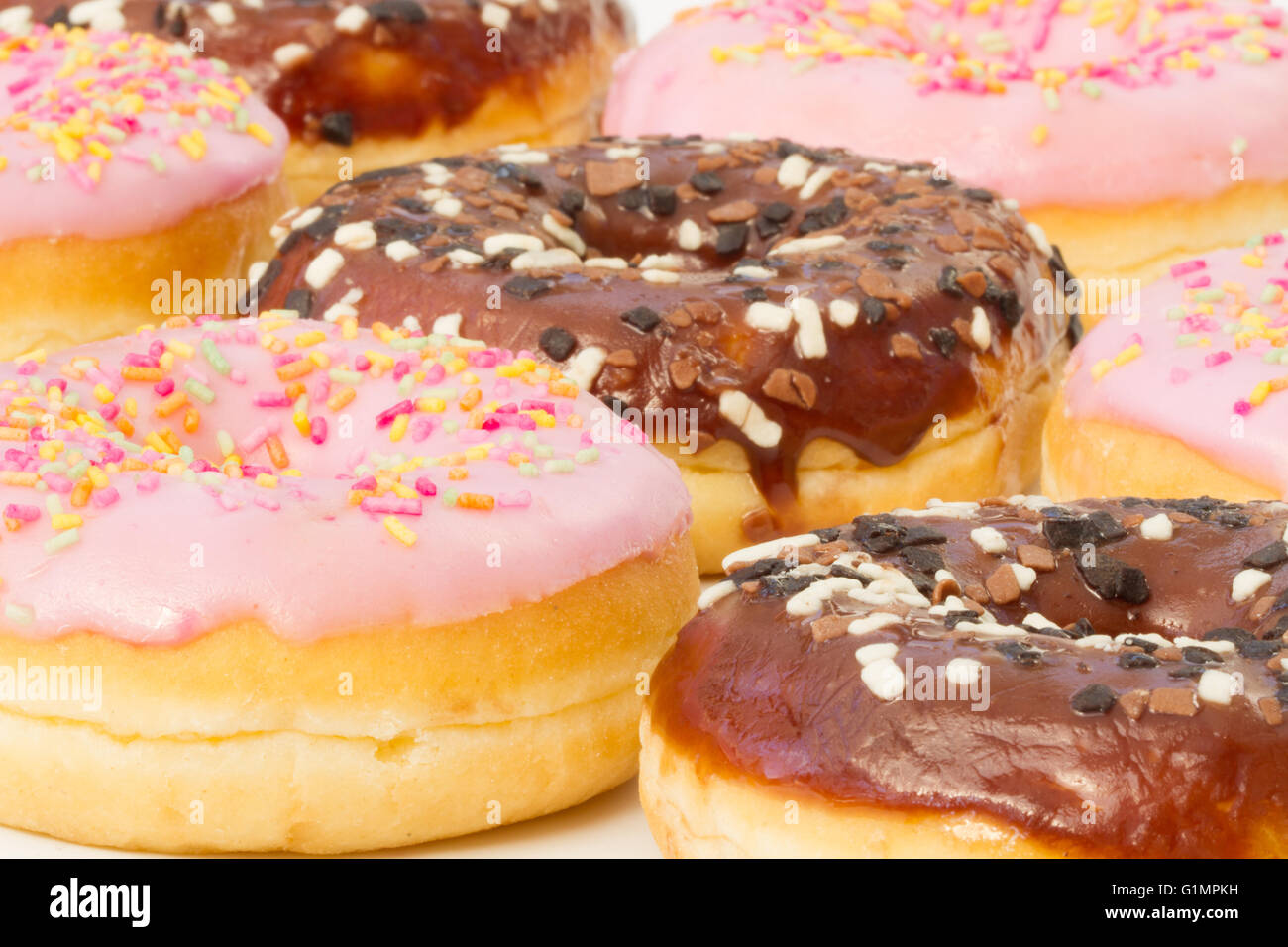Lignes de chocolat et des beignets glacés rose avec un cas isolé sur sprinkles fond blanc. Banque D'Images