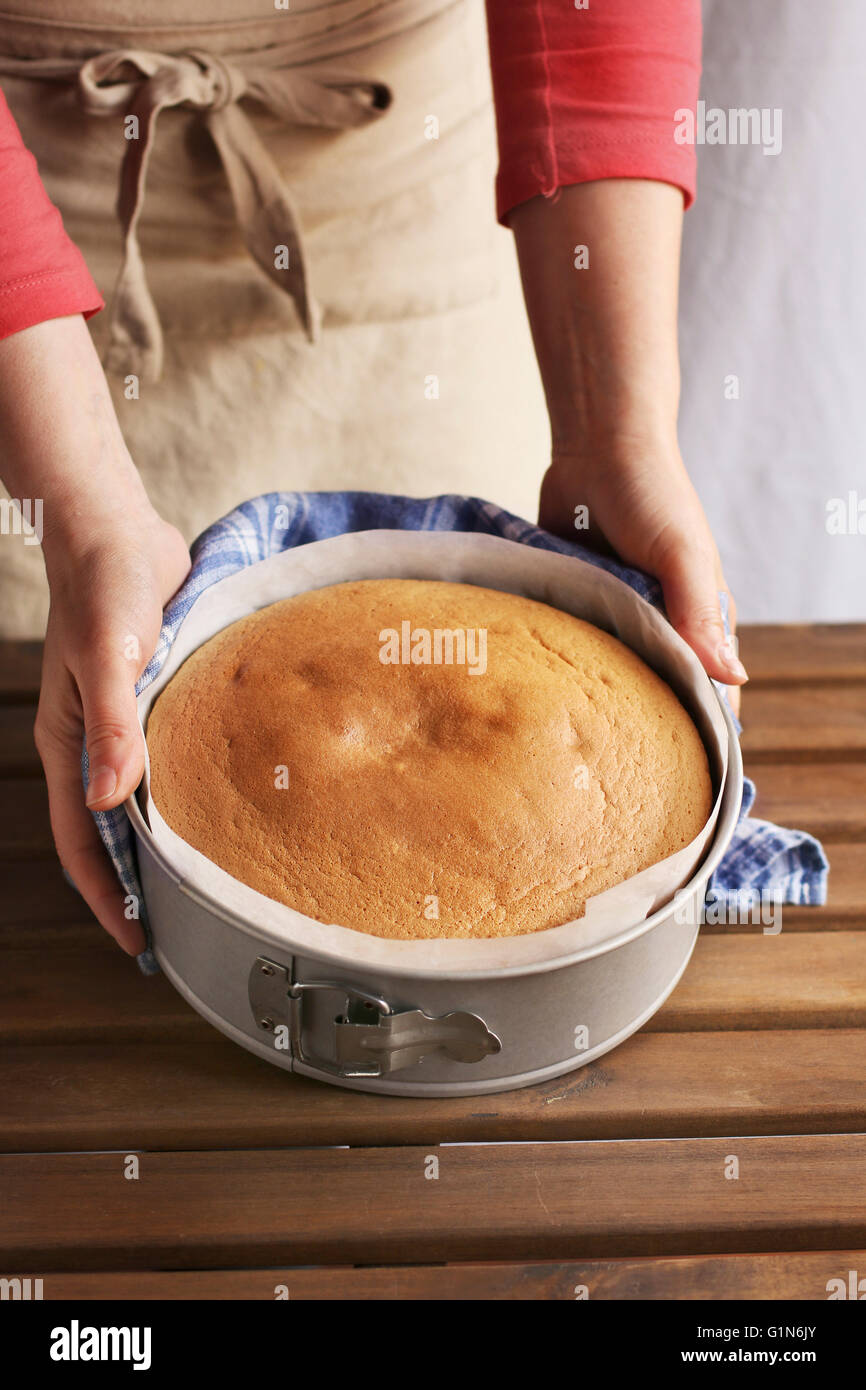 Les mains tenant un gâteau mousseline dans une casserole Banque D'Images