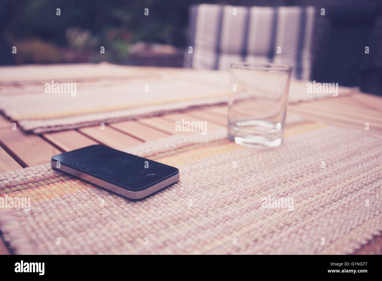 Un téléphone intelligent et un verre vide sur une table à l'extérieur en été Banque D'Images