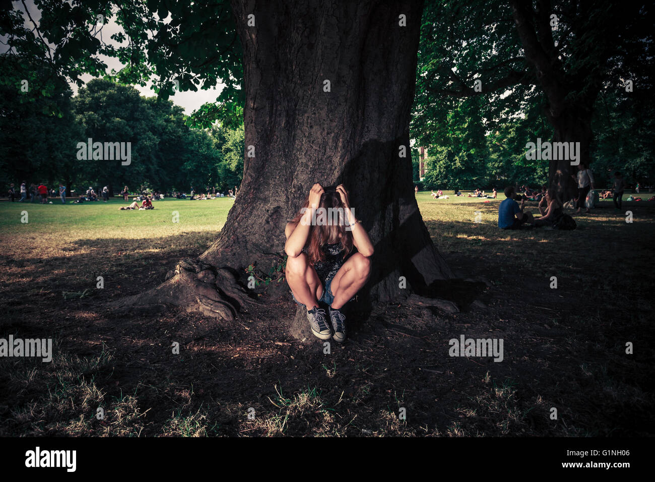Un appui sur une jeune femme fatiguée est assis sous un grand arbre dans le parc Banque D'Images