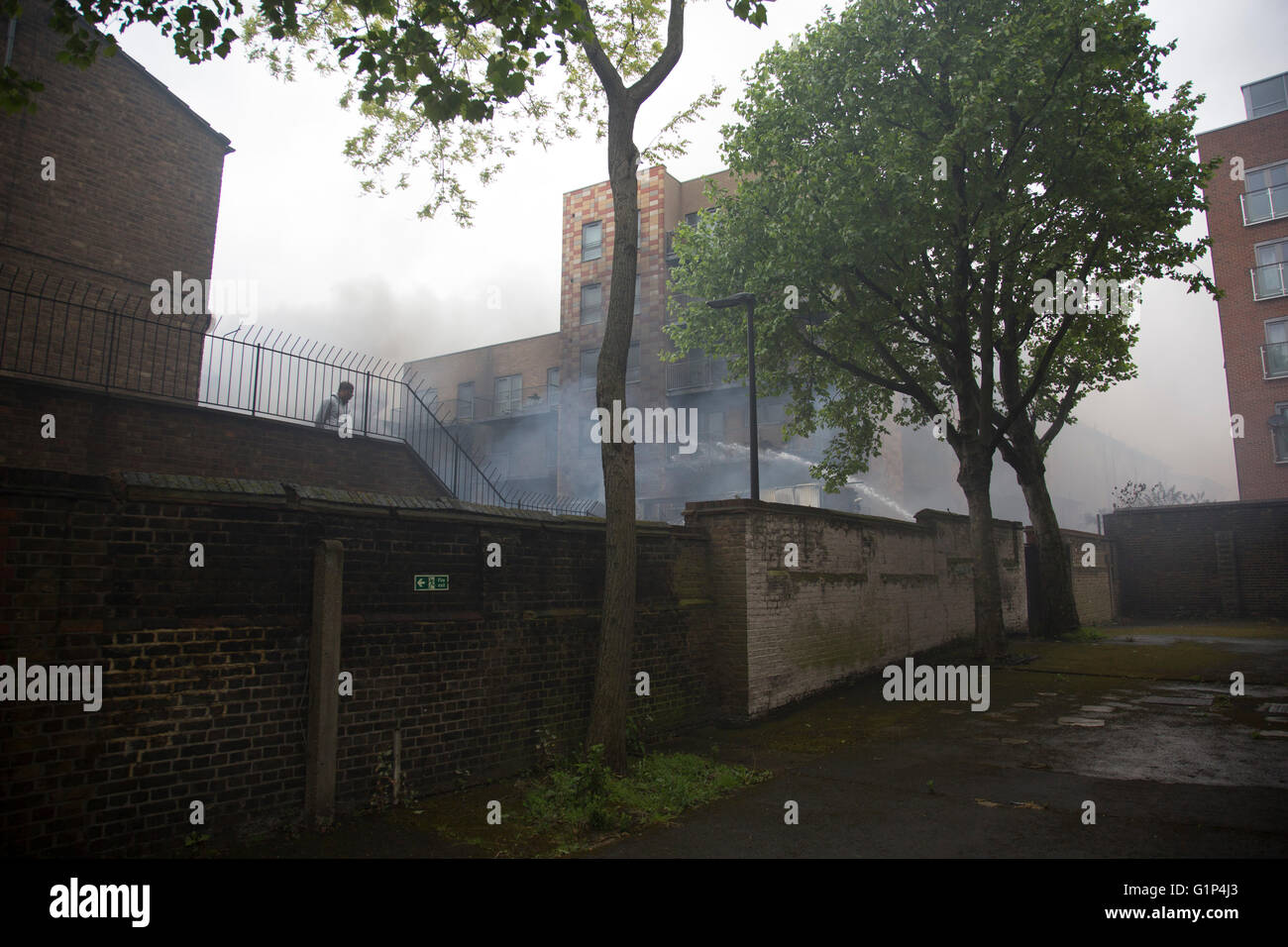 Les habitants regardent le fire Crew s'attaquer à un incendie dans un immeuble d'appartements à Brodlove Lane à Wapping, Londres, Royaume-Uni. Selon les sources, l'incendie était peut-être due à des bouteilles de gaz qui ont été dans une cour de constructeurs à la base du bâtiment. Un résident local a dit qu'il y avait souvent des incendies dans cette région, bien qu'il ne savait pas quelle en était la cause. Banque D'Images