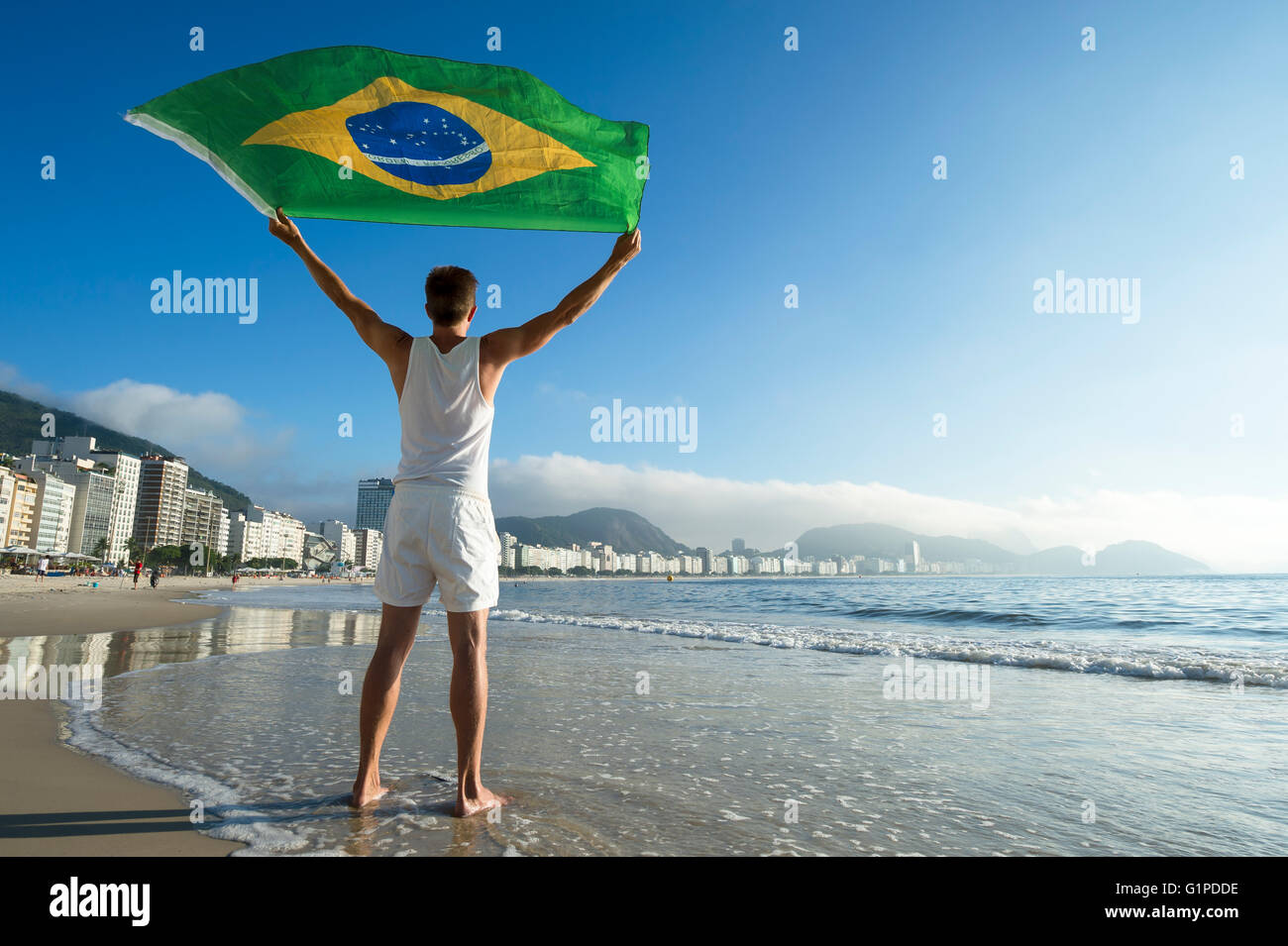 Athlète en tenue blanche avec commandes de brandir le drapeau du Brésil  dans le vent sur les rives de la plage de Copacabana, Rio de Janeiro,  Brésil Photo Stock - Alamy