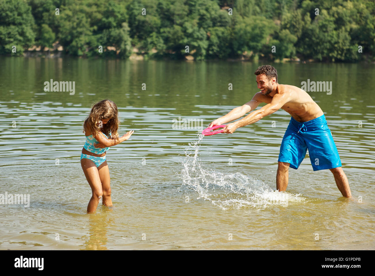 Père et fille éclaboussant les uns les autres avec de l'eau à un lac Banque D'Images