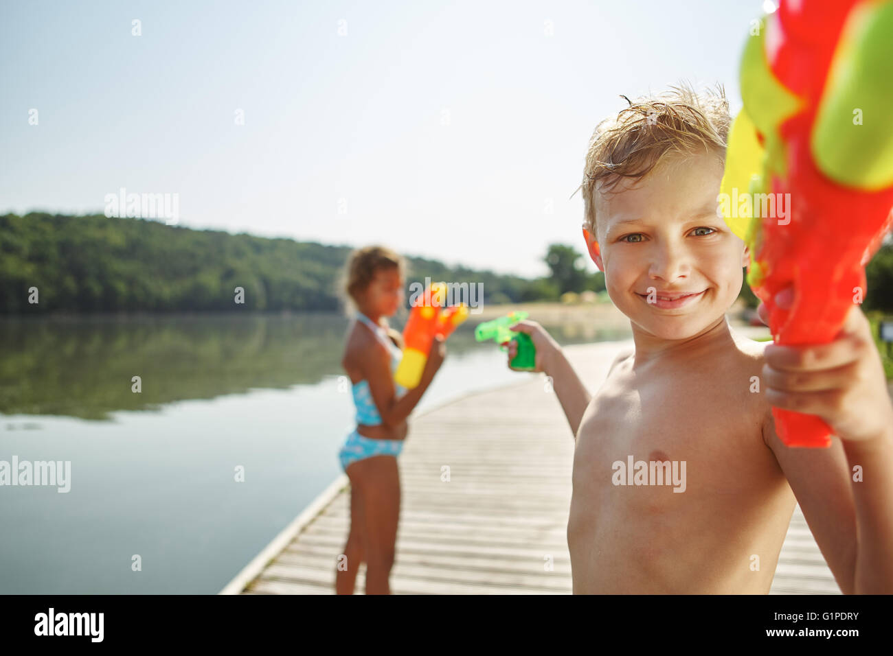 Enfant avec un squirt gun à un lac à sa sœur de pulvérisation avec de l'eau Banque D'Images