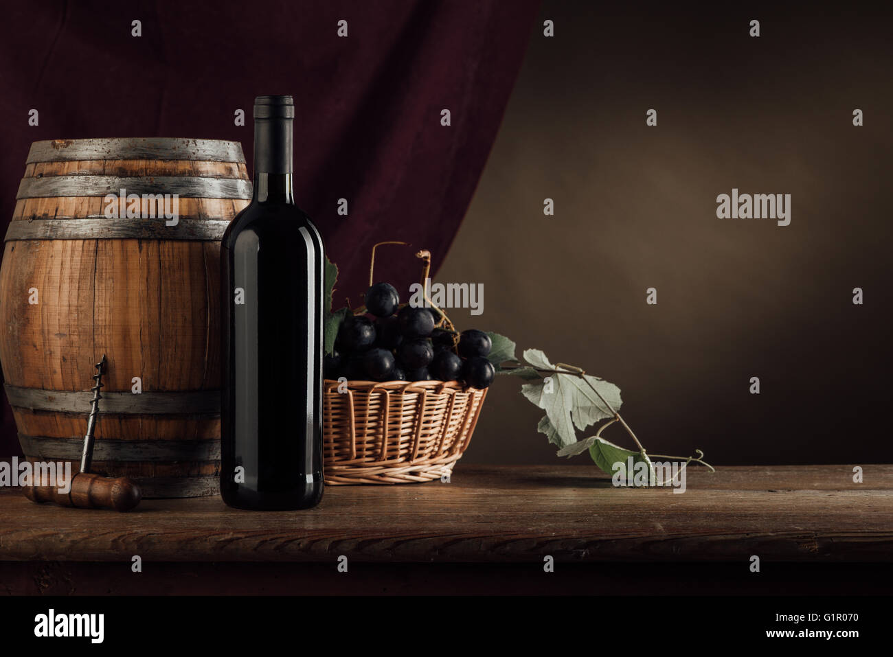 Bouteille de vin rouge, le canon et le panier de raisins sur une table en bois rustique, le drapé rouge sur l'arrière-plan, la dégustation de vins still life Banque D'Images