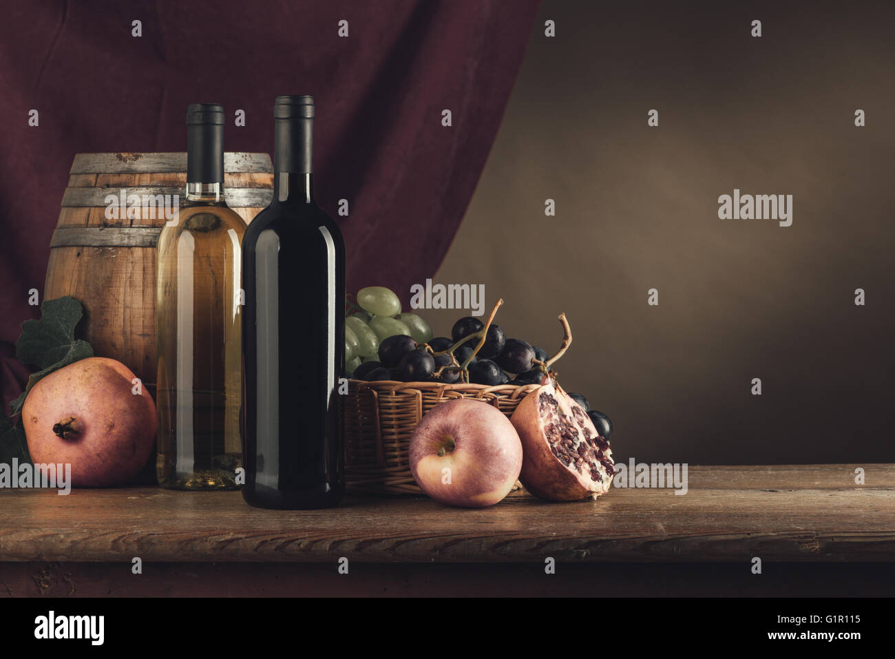 Les bouteilles de vin, le canon et le panier de fruits sur une table en bois rustique, le drapé rouge sur l'arrière-plan, still life Banque D'Images