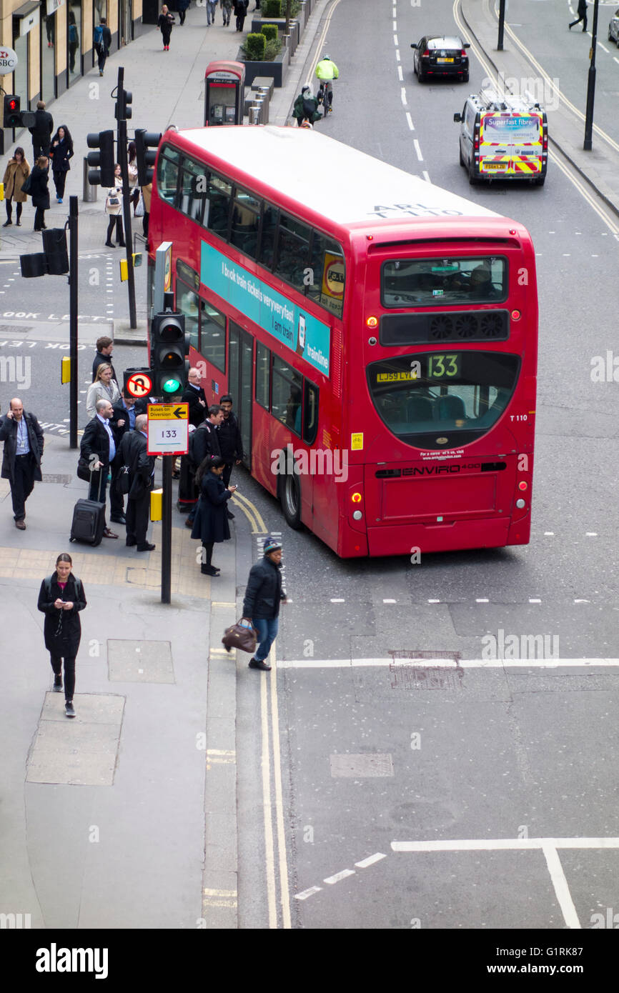 Bus de Londres de tourner à gauche à un carrefour à côté de piétons sur le trottoir Banque D'Images