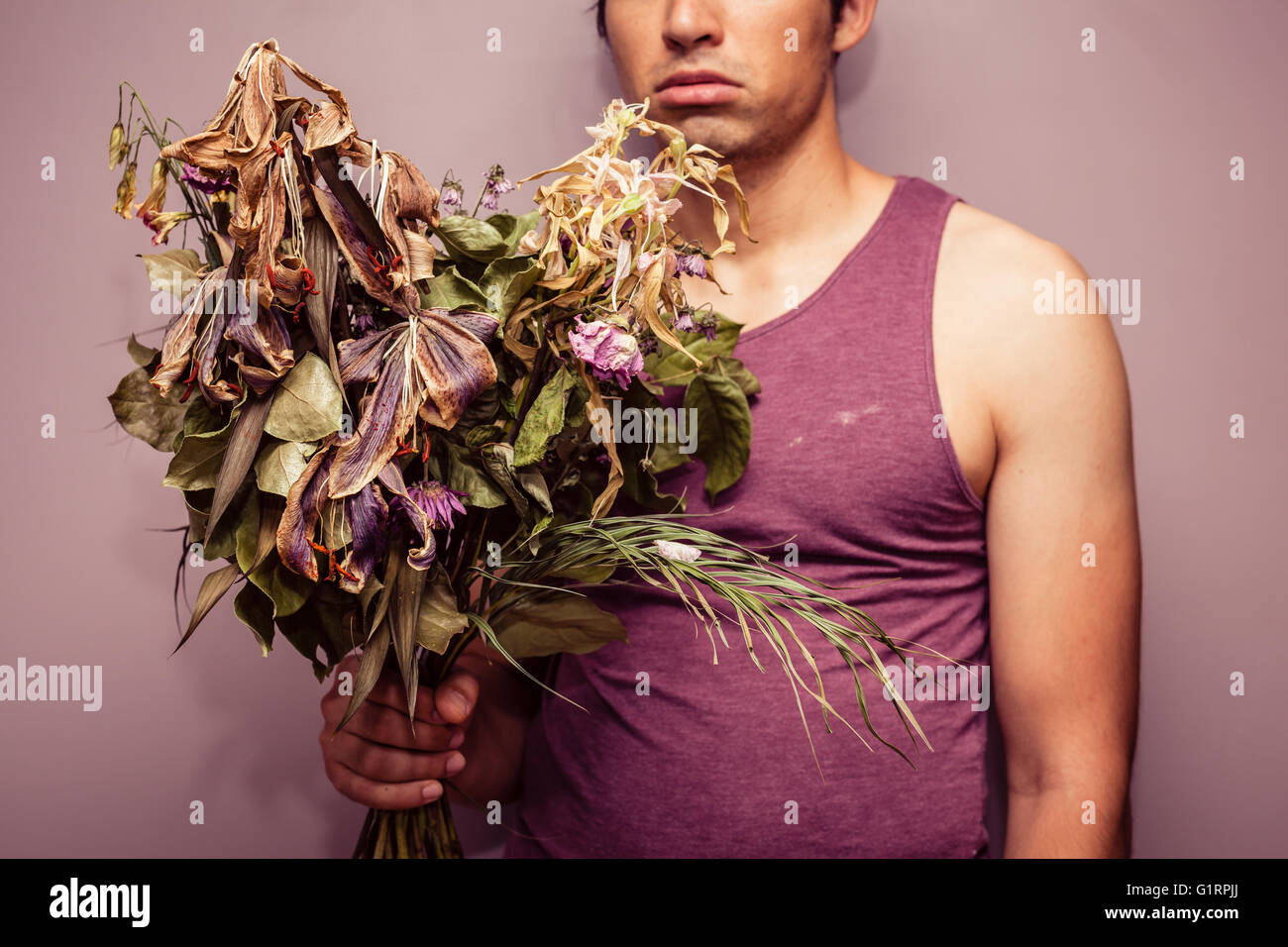 Un jeune homme triste tient un bouquet de fleurs fanées et mortes Banque D'Images