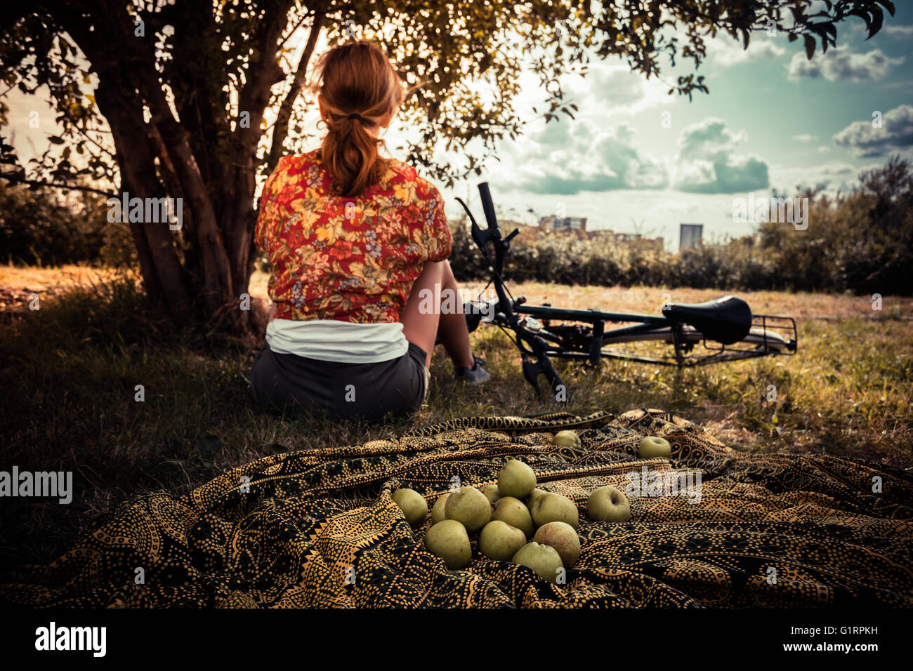 Une jeune femme est assise sous un arbre avec un tas de pommes et un vélo Banque D'Images