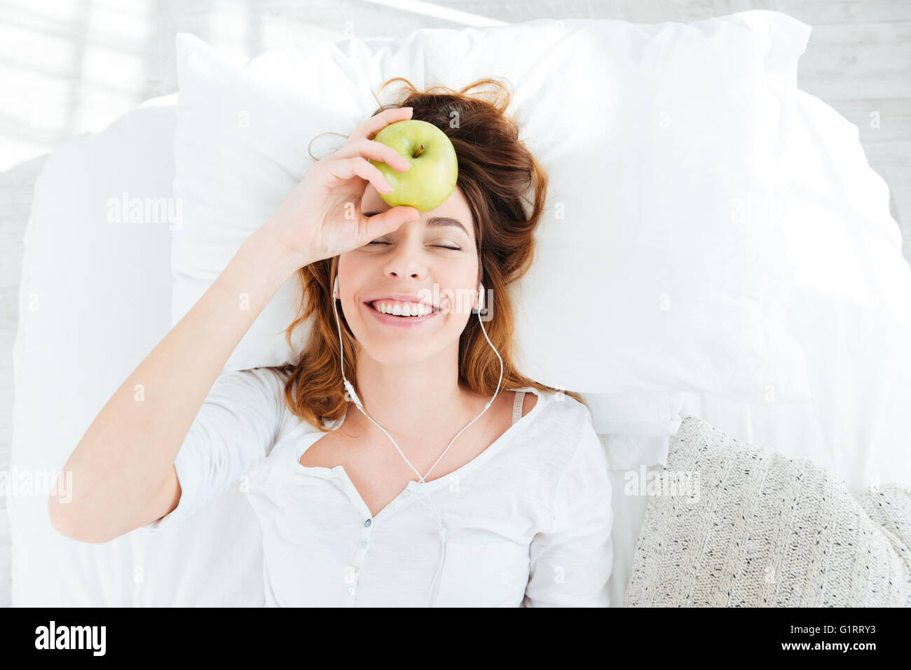 Happy woman holding apple avec des écouteurs sur le lit à la maison Banque D'Images