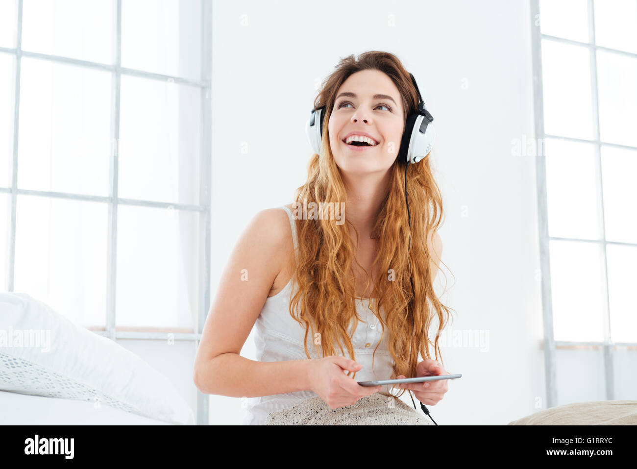Cheerful woman using tablet computer avec écouteurs et à la recherche jusqu'à la maison Banque D'Images