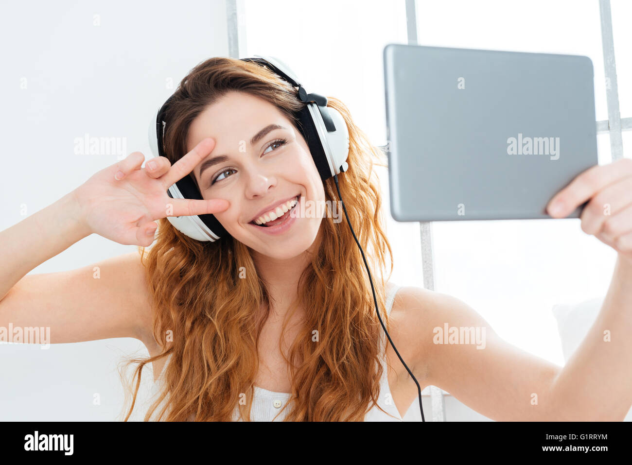 Happy woman in headphones décisions photo selfies sur tablet computer at home Banque D'Images