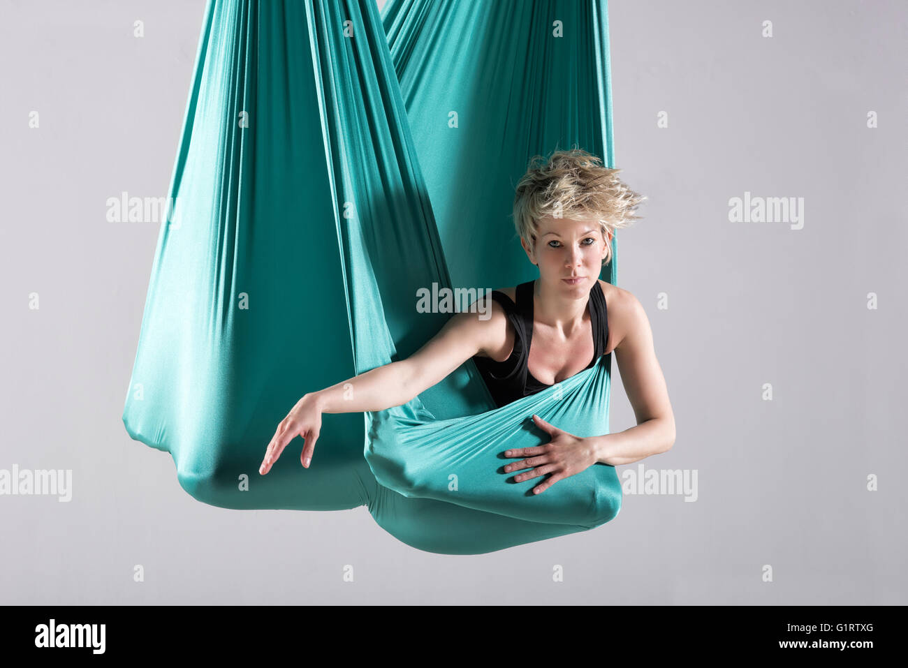 Seule femme athlétique intense faisant des exercices d'étirement de la jambe et de la hanche enveloppé dans une couverture de yoga aérien suspendu du plafond Banque D'Images