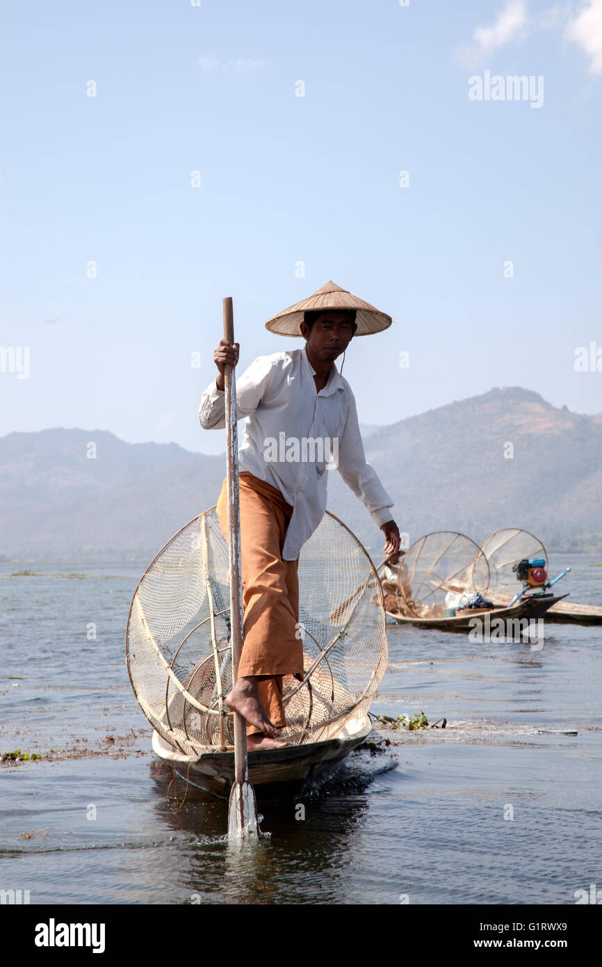 Sur le lac Inle, un pêcheur son bateau à rames avec une jambe sur un mouvement acrobatique (Birmanie). Pêcheur à la nasse sur le lac Inlé. Banque D'Images