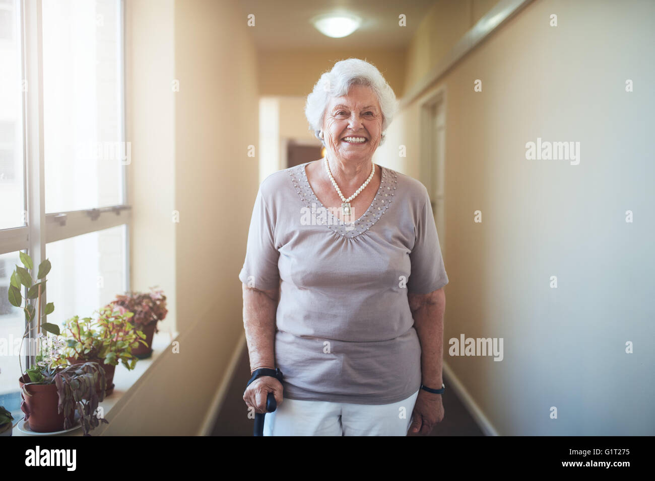 Portrait of senior woman with walking stick debout à la maison. Caucasian female looking at camera et souriant. Banque D'Images