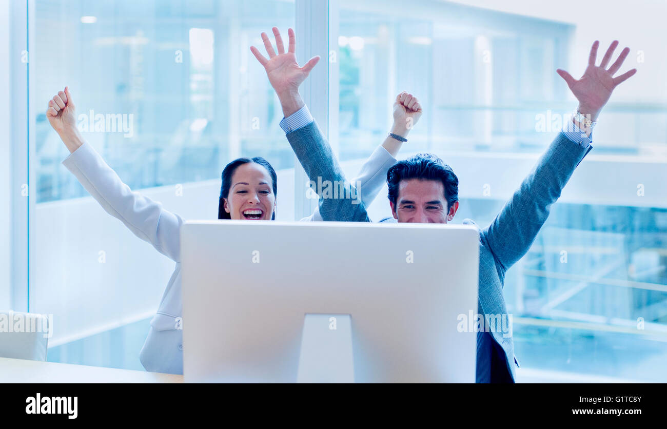 Exubérant businessman and businesswoman cheering with arms raised at computer in office Banque D'Images