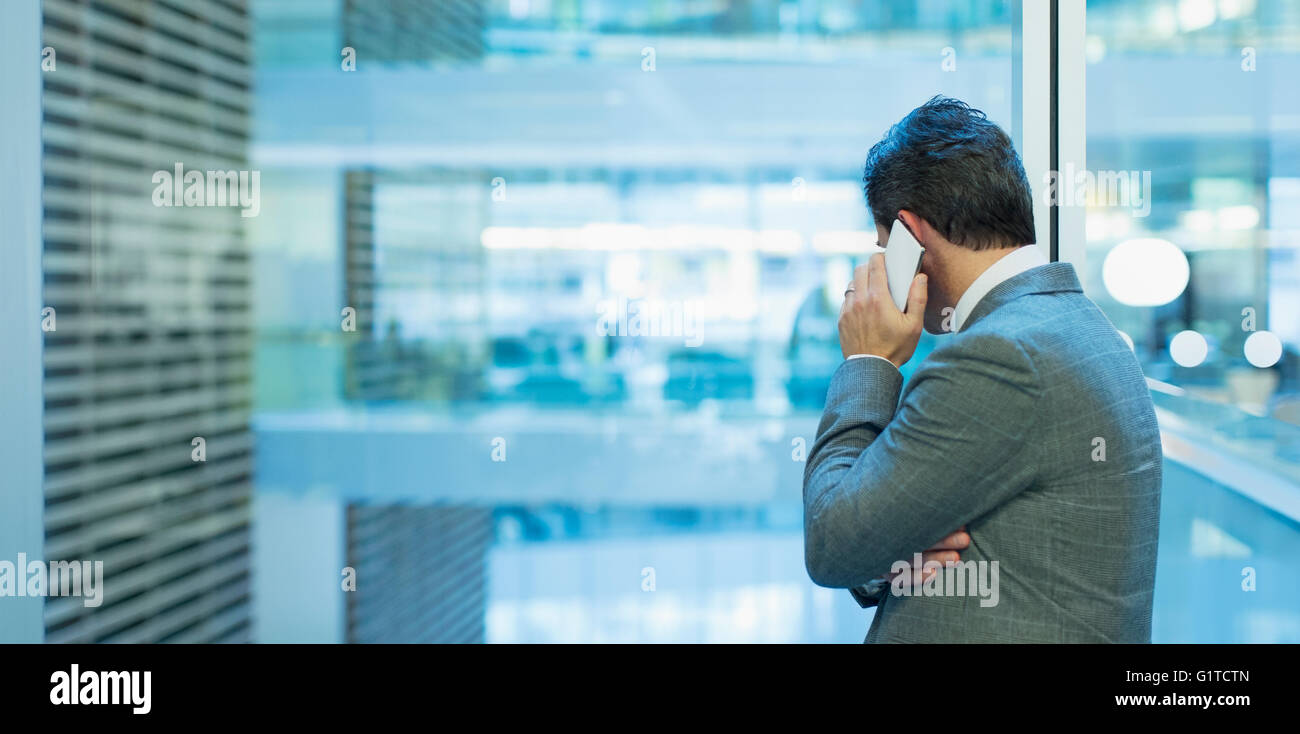 Businessman talking on cell phone at office window Banque D'Images