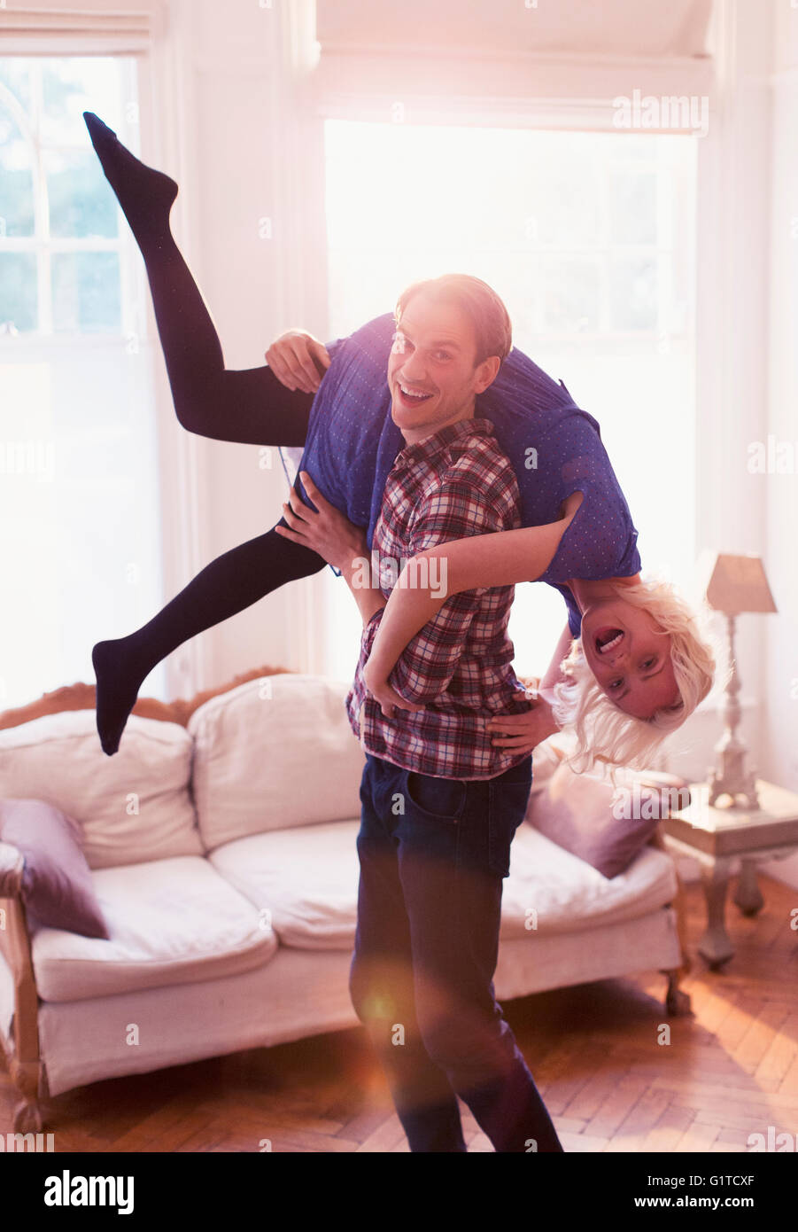 Portrait femme transportant mari espiègle sur l'épaule dans la salle de séjour Banque D'Images