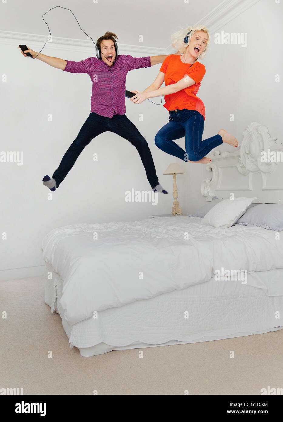 Portrait playful couple jumping on lit et écouter de la musique avec un lecteur mp3 et casque Banque D'Images