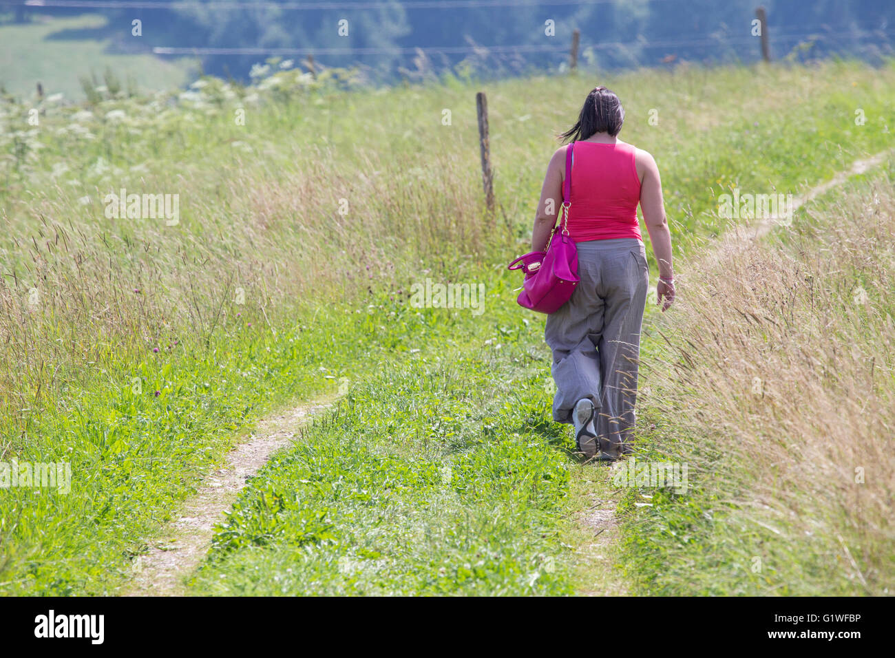 Vue arrière d'une méconnaissable black-haired woman marche sur un sentier chemin dans l'herbe Banque D'Images