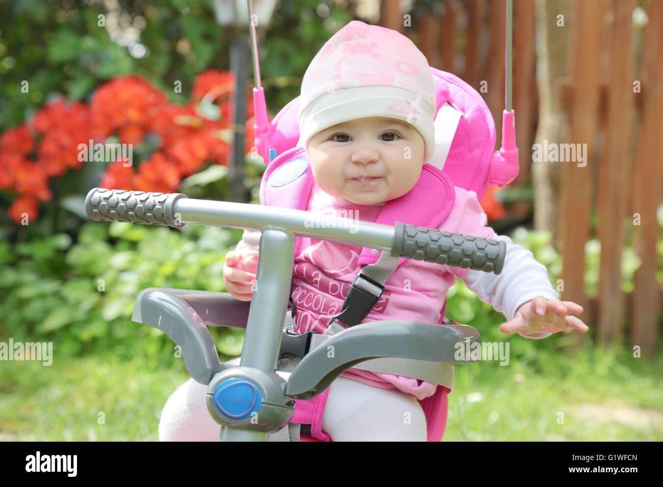 Adorable petite fille de 6 mois sur le jardin en tricycle rose Banque D'Images