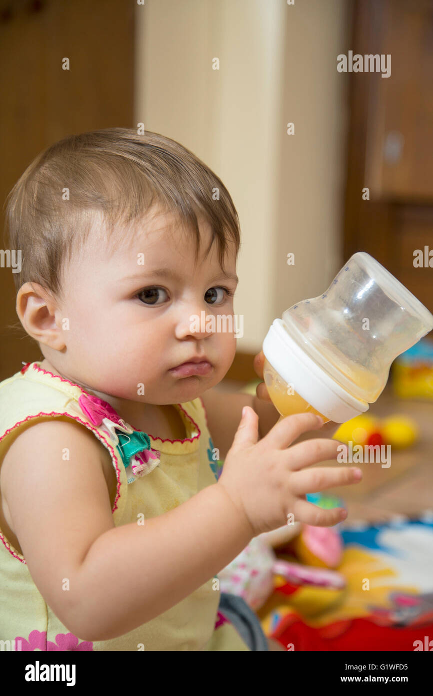 Portrait of cute un an bébé girl looking at camera et tenant une bouteille d'alimentation Banque D'Images