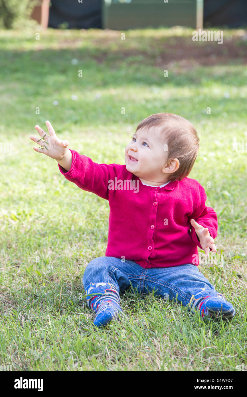 Un an baby girl sitting on grass en souriant avec de l'herbe dans la main Banque D'Images