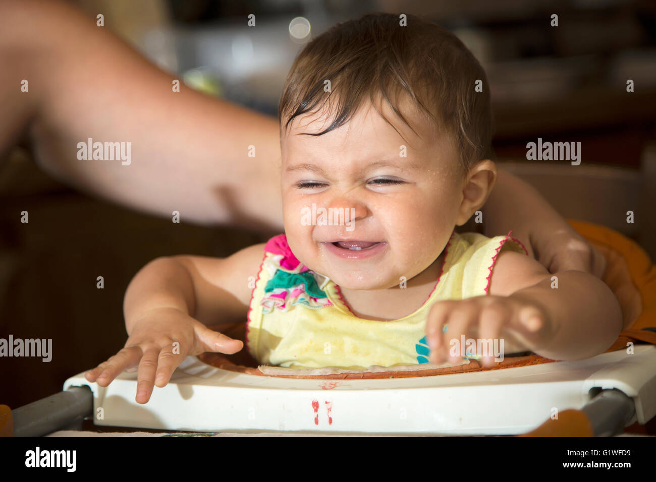 Portrait d'un jeune de l'année les yeux plissés en souriant sur une chaise de bébé avec le visage mouillé Banque D'Images
