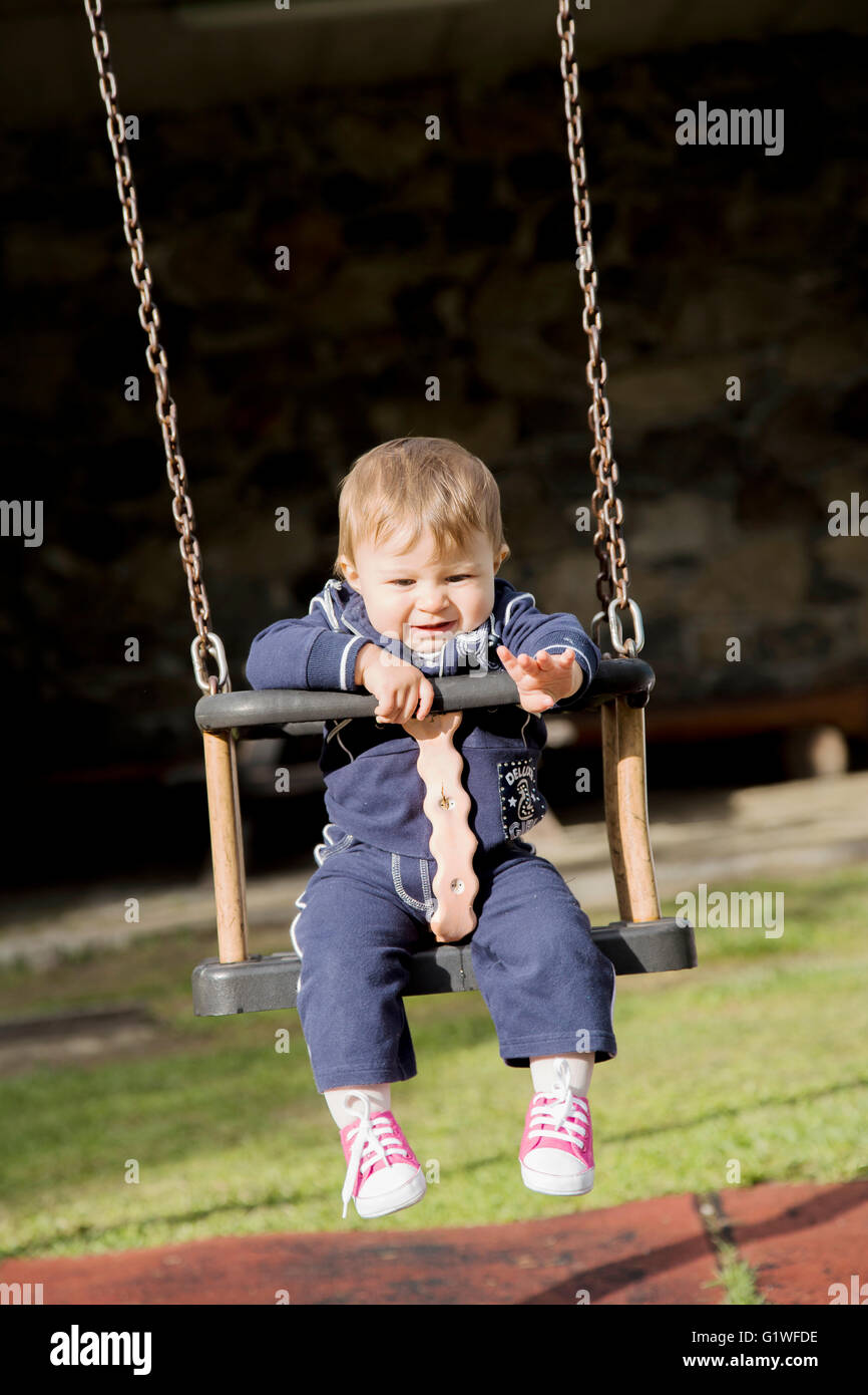 Portrait de peu d'un an baby girl on swing tirant son bras tout en regardant vers le bas Banque D'Images