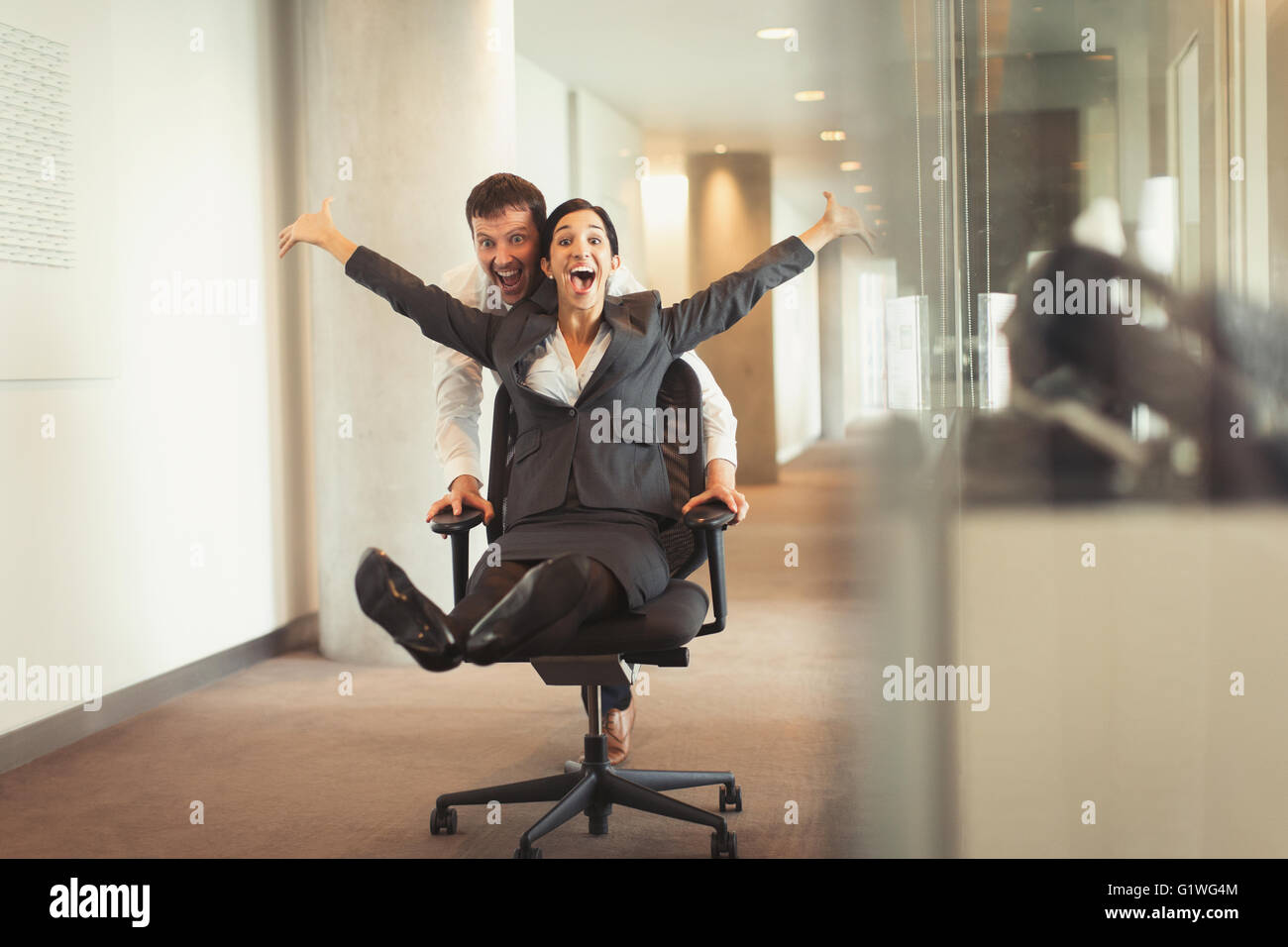 Businessman pushing ludique femme exubérante down corridor en chaise de bureau Banque D'Images