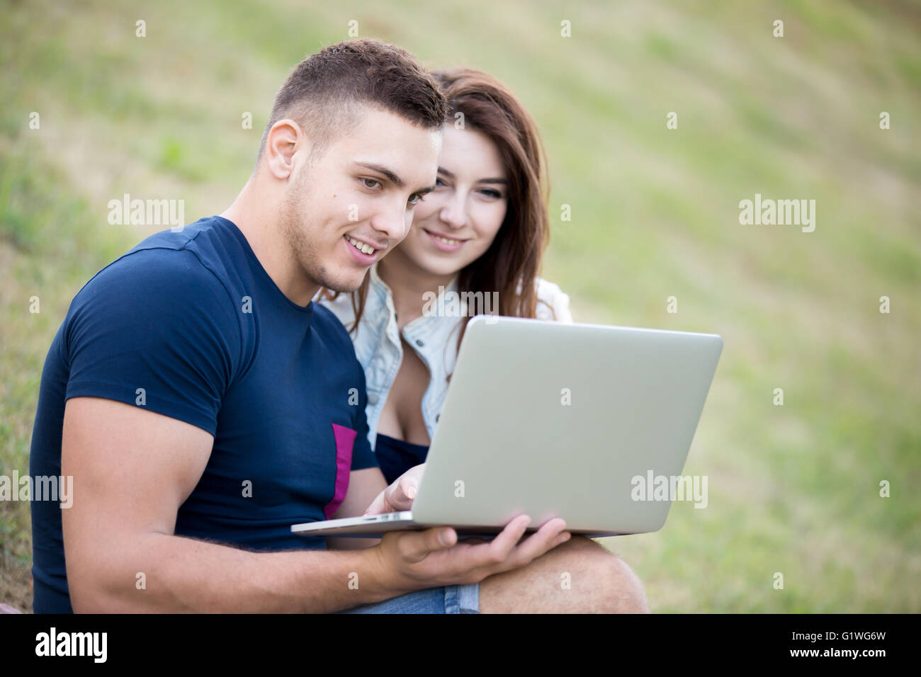 Portrait de jeune homme positif et smiling Beautiful woman in casual clothes sitting on grass in park sur journée d'été Banque D'Images
