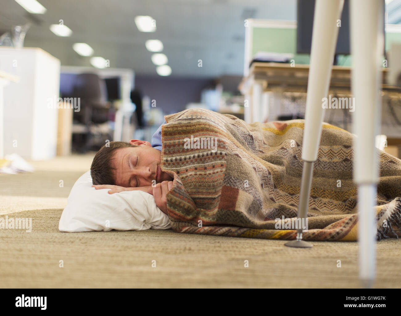 Businessman avec oreiller et couverture dormir sur plancher de bureau Banque D'Images