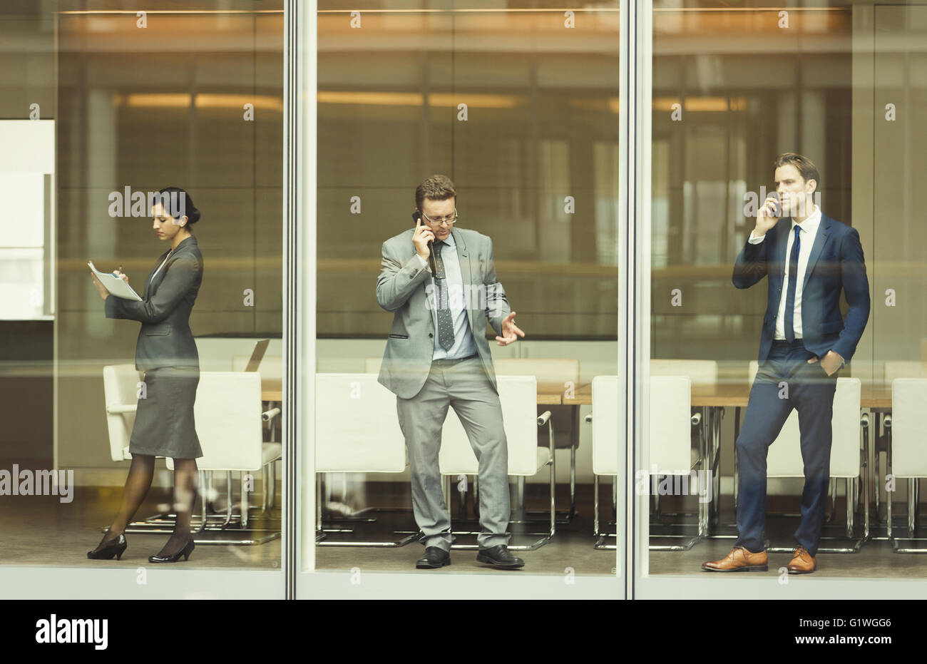 Les gens d'affaires sur les téléphones cellulaires et la prise de notes à la fenêtre de la salle de conférence Banque D'Images
