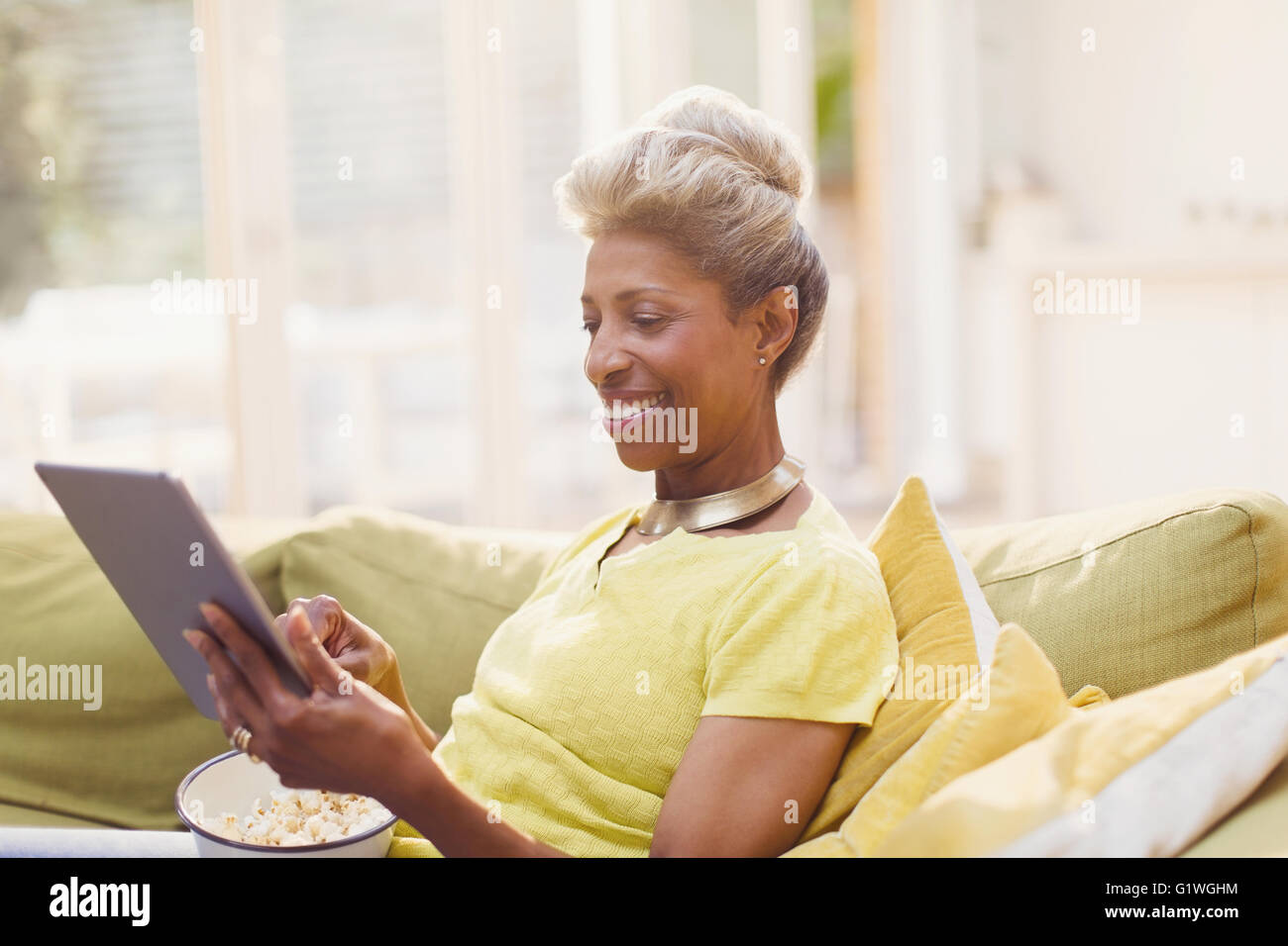 Les femmes mûres using digital tablet eating popcorn sur canapé Banque D'Images