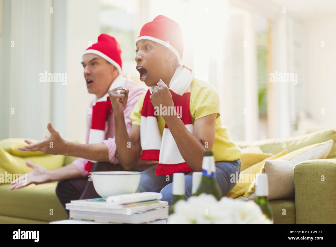 Cheering couple matching chapeaux et regarder la télévision dans le salon de l'événement sportif Banque D'Images