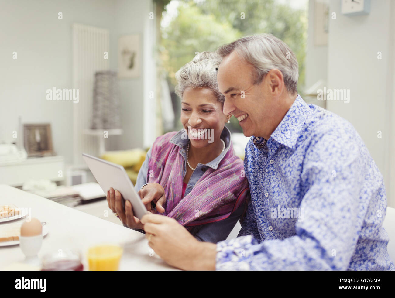 Smiling mature couple sharing digital tablet at breakfast table Banque D'Images