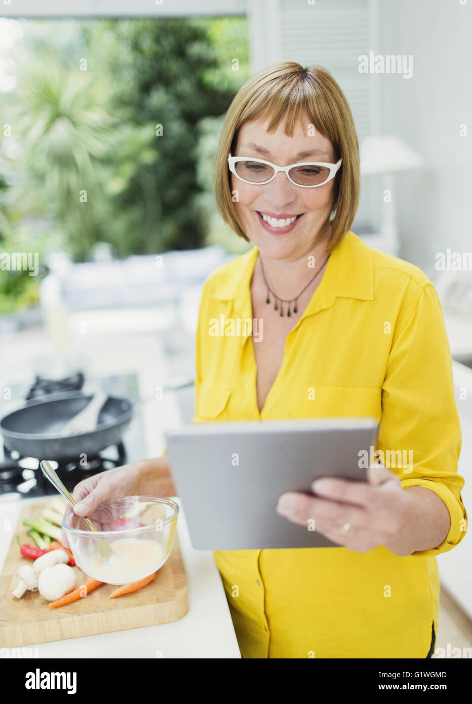 Smiling mature woman using digital tablet et la cuisson dans la cuisine Banque D'Images